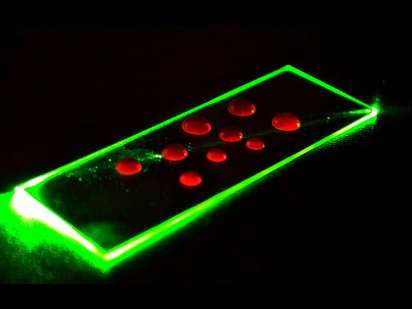 La lumi&egrave;re issue d'un laser vert est guid&eacute;e dans une lame de verre ce qui permet de stimuler la fluorescence de fluorophores pr&eacute;sents dans les gouttes distribu&eacute;es sur la surface.